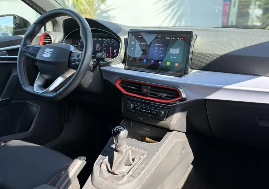 Vue intérieure côté conducteur du tableau de bord et console centrale d'une SEAT IBIZA TSI 115 FR avec détails rouges et écran tactile.