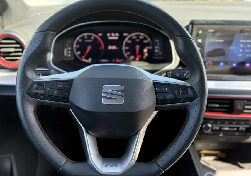 Vue rapprochée du volant perforé noir avec surpiqûres rouges et tableau de bord digital de la SEAT Ibiza TSI 115 FR 2025.
