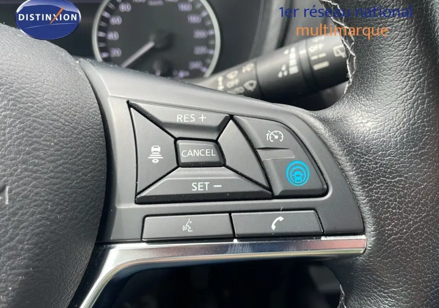 Gros plan sur les commandes au volant d'un Nissan Juke Hybrid 2023 gris perle, avec régulateur de vitesse et fonctions vocales.