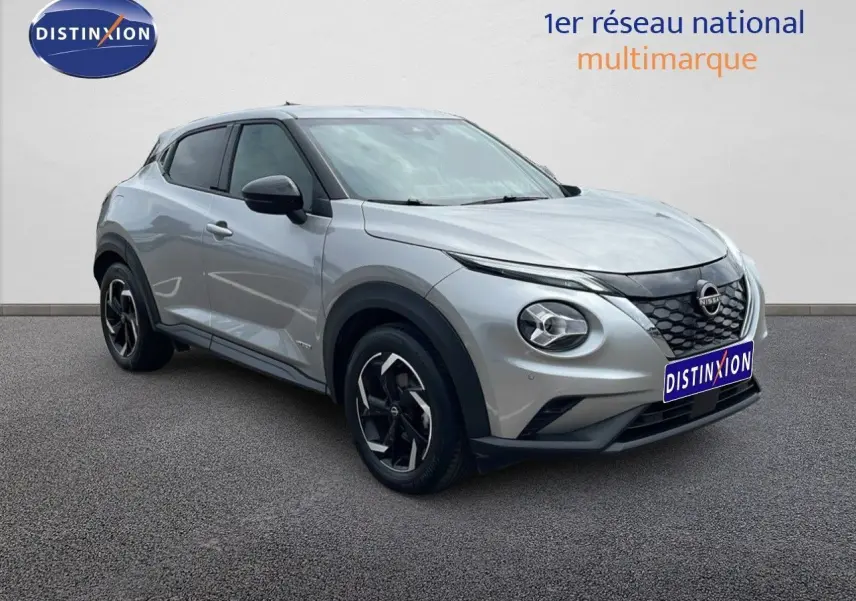 Nissan Juke Hybrid gris perle métal vu en 3/4 avant droit, avec jantes noires et calandre distinctive.