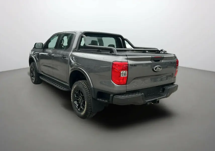 Ford Ranger 2025 gris carbone en vue 3/4 arrière droit, avec benne et barres de protection noires visibles.