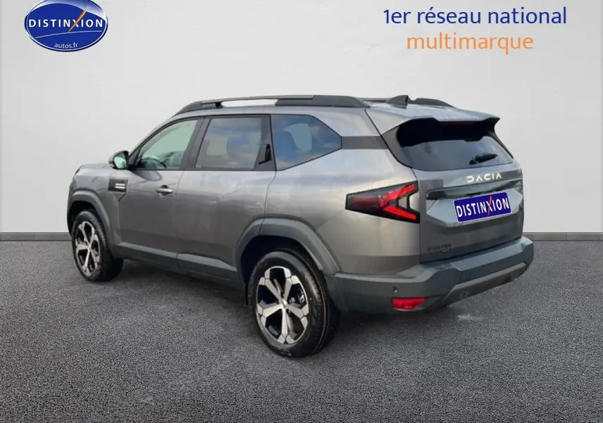 Vue 3/4 arrière droite du SUV Dacia Bigster gris schiste avec jantes diamantées et barres de toit noires.