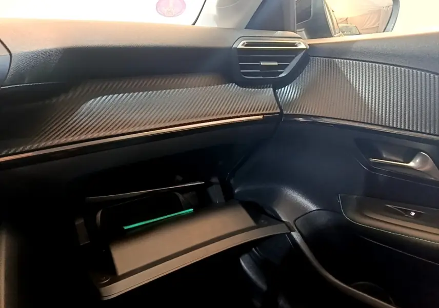 Vue intérieure côté passager du tableau de bord noir avec insert effet carbone et boîte à gants ouverte du Peugeot 208 jaune.