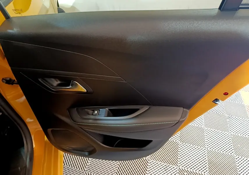 Vue rapprochée de la porte arrière gauche noire avec surpiqûres, sur Peugeot 208 jaune 2023.