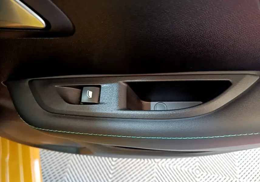 Gros plan sur la commande de lève-vitre côté conducteur avec surpiqûre bleue sur la porte noire d’une Peugeot 208 jaune.