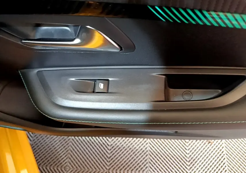 Gros plan sur la poignée intérieure côté gauche de la porte noire avec surpiqûres vertes d’une Peugeot 208 jaune.