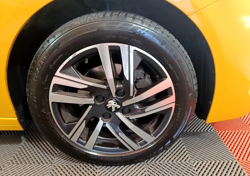 Gros plan sur la roue avant droite d'une Peugeot 208 jaune 2023 avec jante alliage bicolore et logo lion.