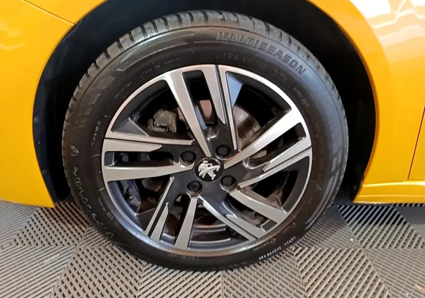 Gros plan sur la roue avant droite de la Peugeot 208 jaune avec jante alliage bicolore et logo lion central.