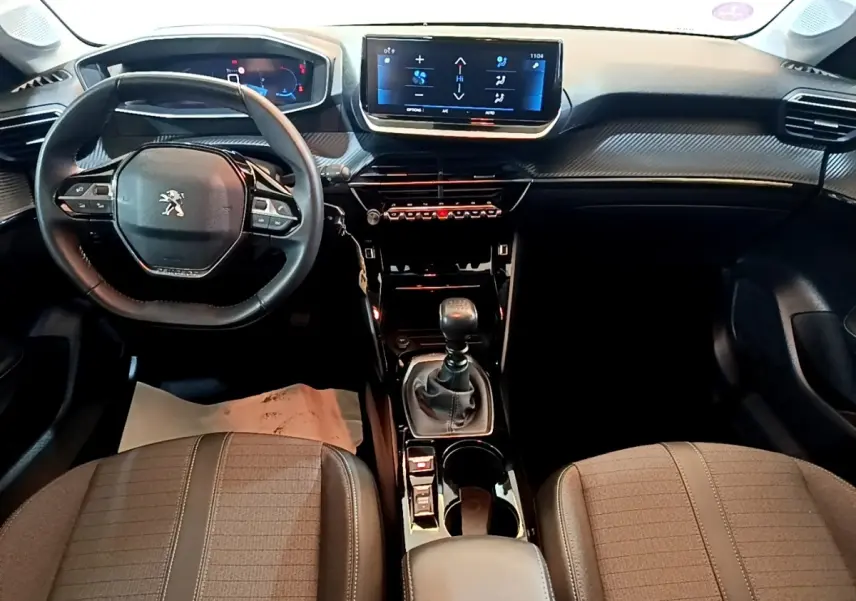 Vue intérieure avant de la Peugeot 208 PureTech 100 S&S Allure Pack 2023, volant cuir multifonctions et écran tactile central.