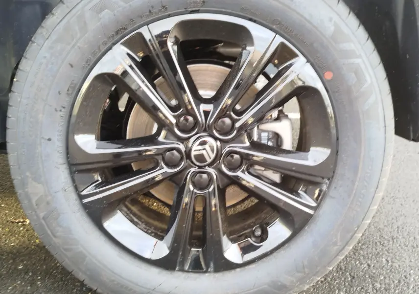 Gros plan sur la jante noire brillante avec logo Citroën au centre, entourée d'un pneu tout-terrain gris.
