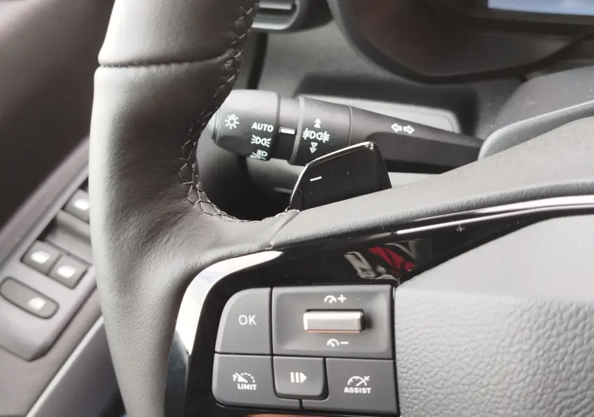 Gros plan sur la partie gauche du volant gris foncé du Citroën Berlingo 2025 avec commandes de régulateur et commodo d’éclairage.