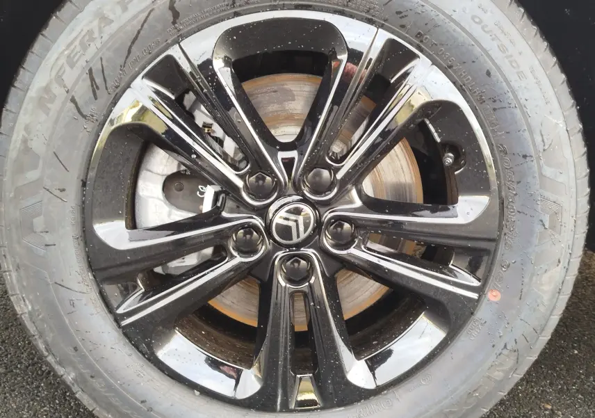 Gros plan sur la jante noire brillante avec logo Citroën au centre, montée sur un pneu gris acier du Berlingo 2025.