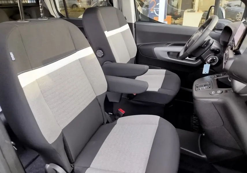 Vue intérieure côté conducteur du Citroën Berlingo 2025, sièges gris bicolores avec accoudoirs et tableau de bord moderne.