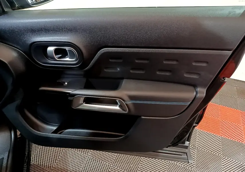 Gros plan sur la porte intérieure côté gauche du Citroën C5 Aircross hybride rechargeable 2022, avec poignée argentée et surpiqûres bleues.