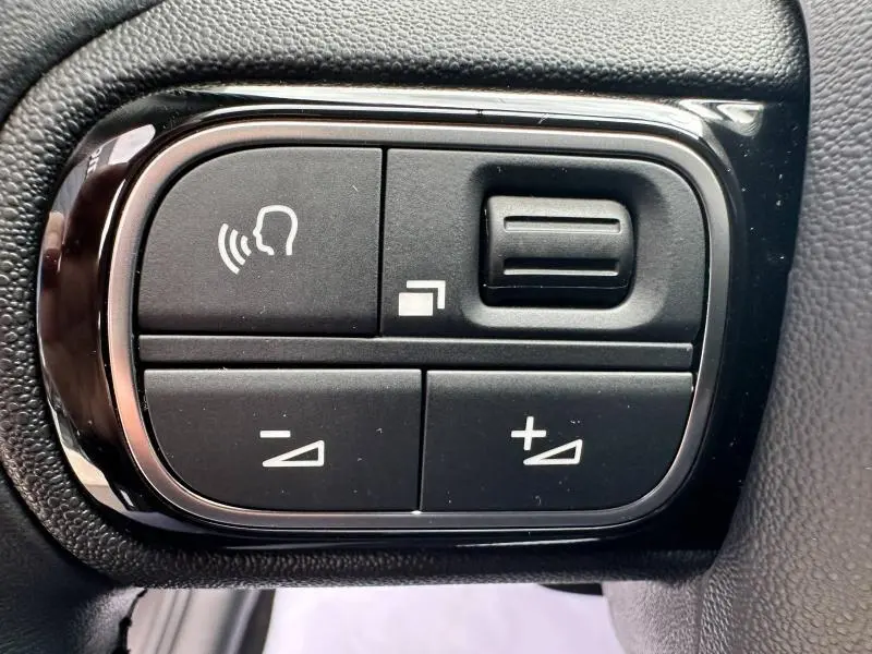 Gros plan sur les commandes vocales et de réglage du volume noires encadrées de chrome dans une Citroën C3 Aircross 2021.
