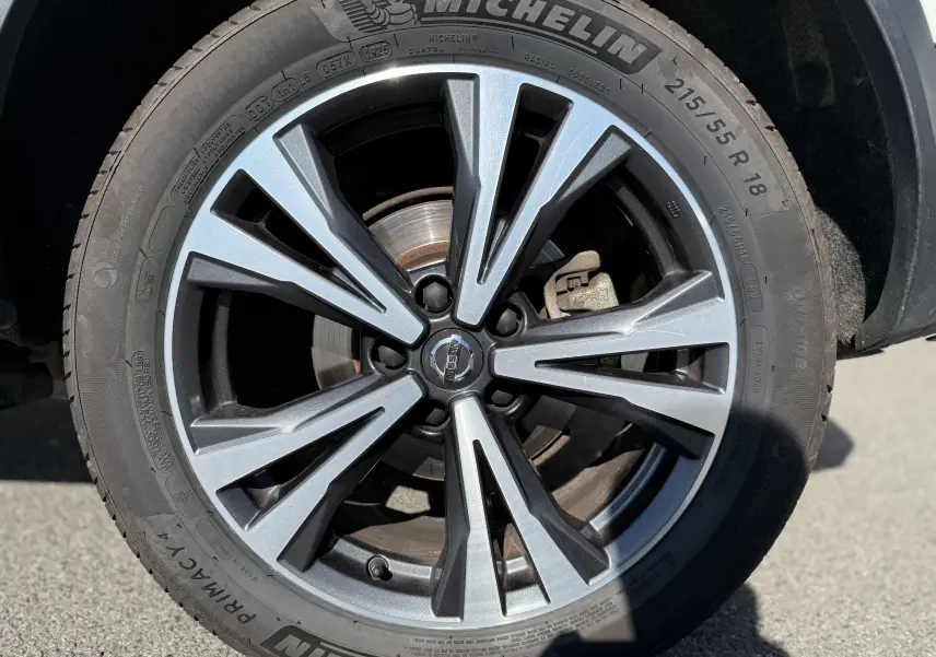 Gros plan sur la jante alliage biton noir et argent du Nissan Qashqai blanc, mettant en valeur le logo central Nissan.