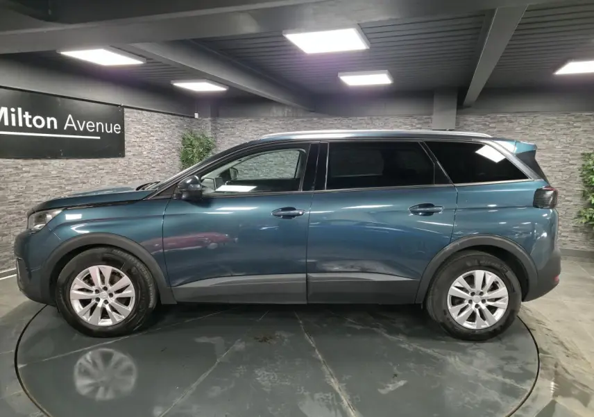 Profil côté gauche du Peugeot 5008 bleu métallisé 2019 avec jantes alliage et vitres surteintées en intérieur showroom.