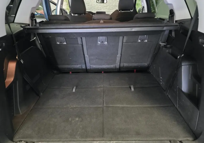 Coffre spacieux du Peugeot 5008 bleu vu de l'arrière avec sièges arrière relevés et cache-bagages noir.