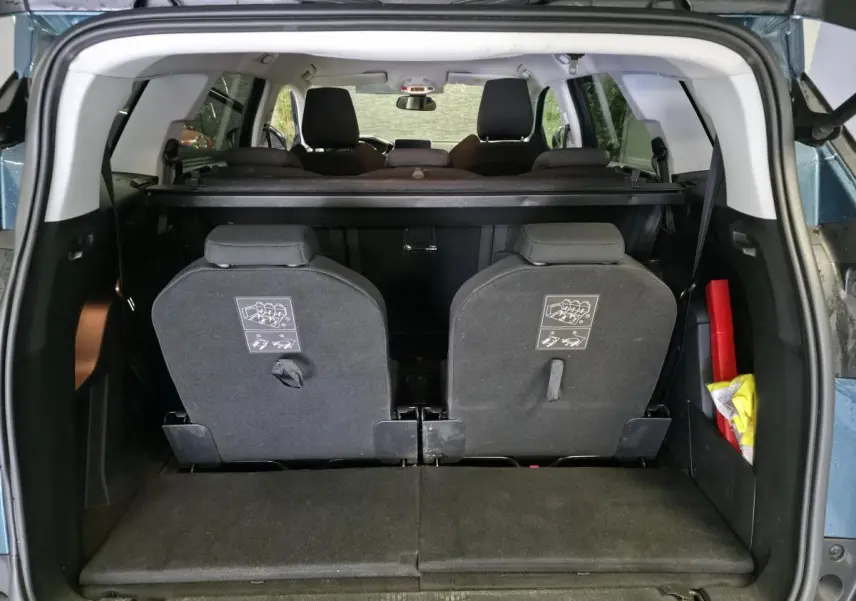 Vue arrière du coffre ouvert d'un Peugeot 5008 bleu 2019, montrant les sièges escamotés du troisième rang et un triangle de sécurité.