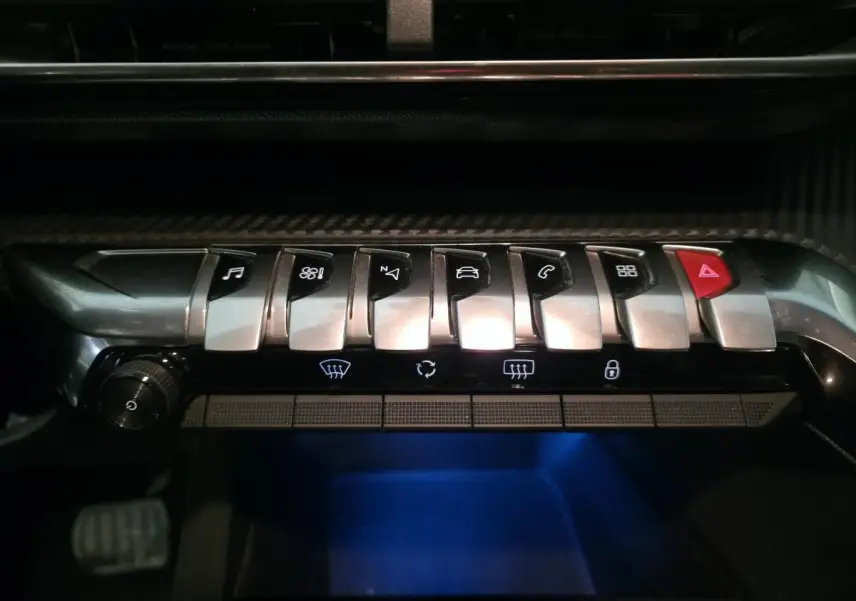 Gros plan sur la rangée de boutons chromés du tableau de bord du Peugeot 5008 bleu, avec éclairage bleu en dessous.