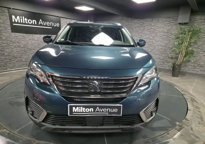 Vue frontale d'un Peugeot 5008 bleu métallisé avec calandre chromée et phares halogènes dans un showroom.
