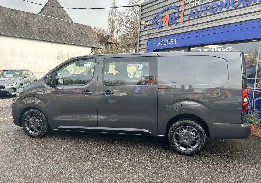 Vue de profil côté gauche d'un Citroën Jumpy Cabine Approfondie gris titane métal, stationné devant un bâtiment commercial.