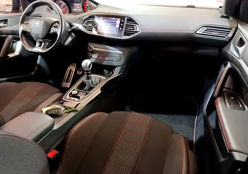 Vue intérieure côté conducteur de la Peugeot 308 GT Line 2016, montrant tableau de bord, volant cuir et écran tactile central.
