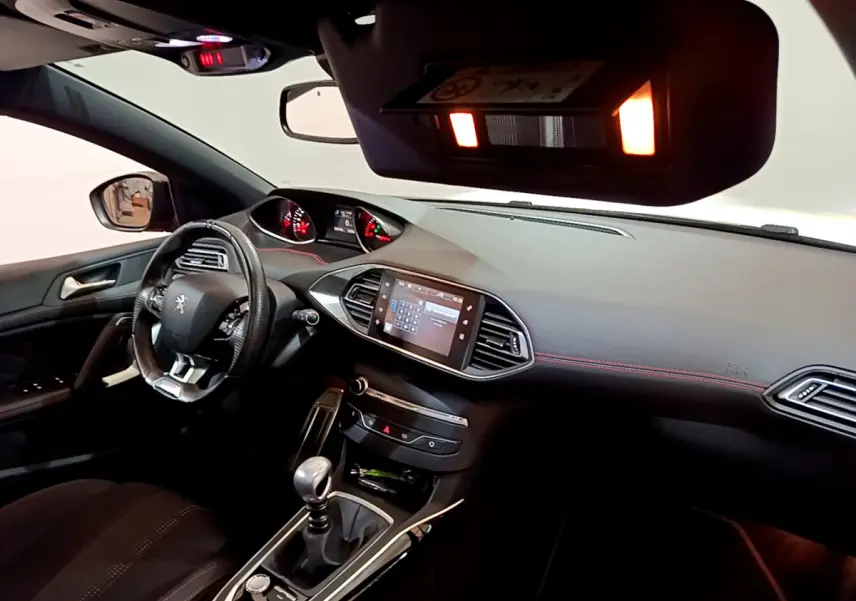 Vue intérieure côté conducteur de la Peugeot 308 gris foncé, mettant en valeur le tableau de bord et la console centrale avec écran tactile.