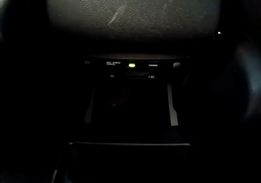 Détail de la prise 12V et prise secteur 230V 120W dans l'habitacle sombre d'une Peugeot 308 gris foncé.