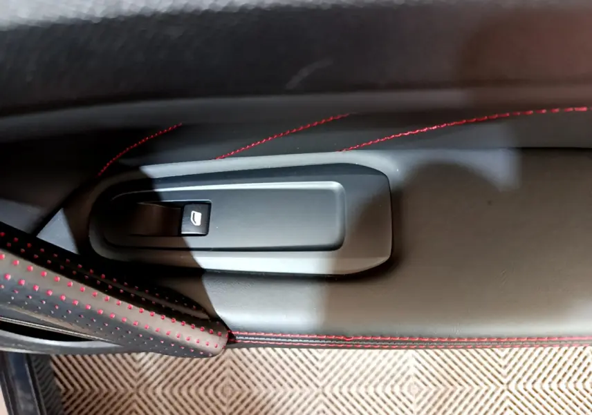 Détail de la commande de lève-vitre sur la porte intérieure droite avec surpiqûres rouges sur cuir noir.