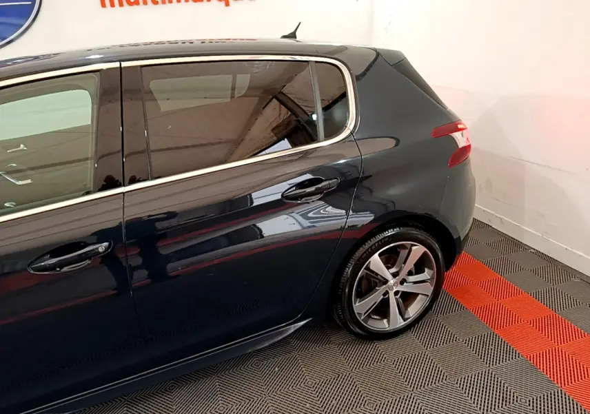 Vue latérale droite d'une Peugeot 308 gris foncé avec jantes alliage et vitres teintées dans un showroom.