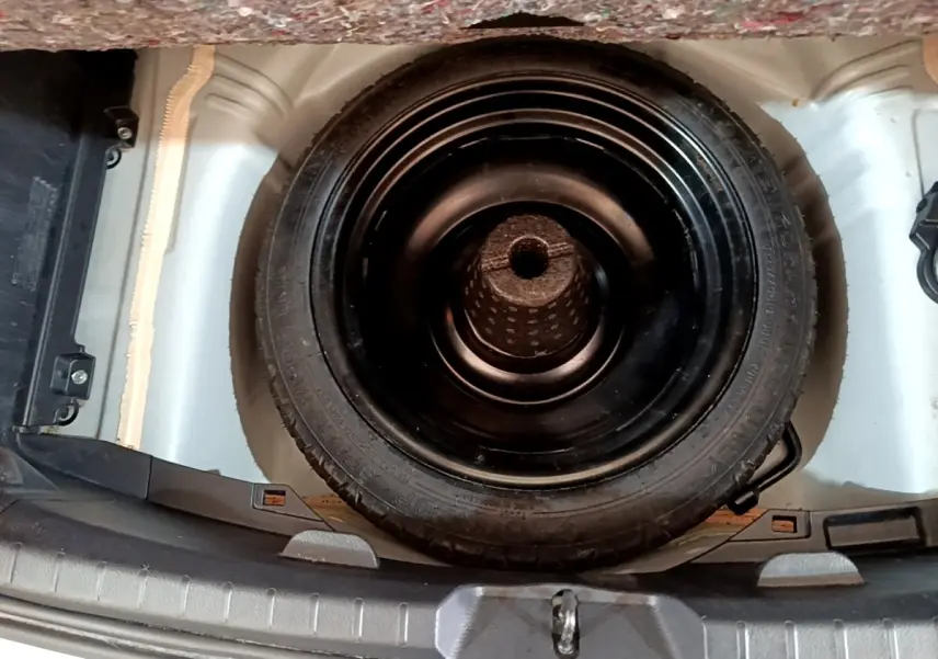 Vue plongeante sur la roue de secours noire logée dans le coffre blanc d'une Toyota Yaris blanche.