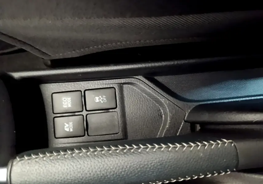 Gros plan sur le frein à main en cuir noir avec surpiqûres blanches et les boutons de modes de conduite d'une Toyota Yaris blanche.