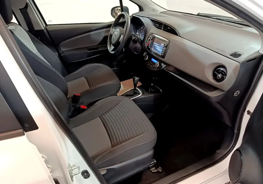Intérieur avant droit d’une Toyota Yaris blanche 2019, montrant sièges noirs, volant multifonctions et tableau de bord avec écran tactile.