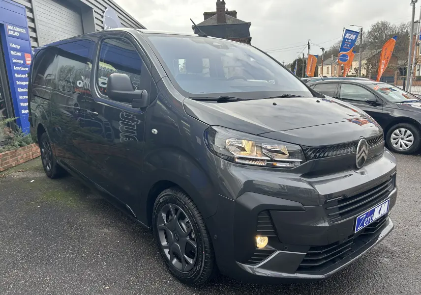 Vue 3/4 avant gauche d'un Citroën Jumpy Cabine Approfondie gris titane métal avec phares allumés sur parking.