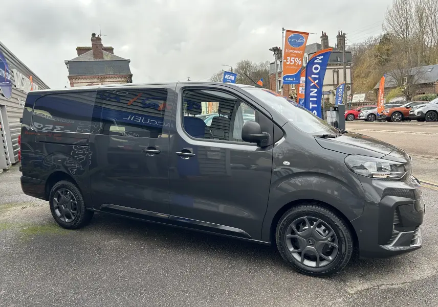 Vue de profil côté gauche d'un Citroën Jumpy cabine approfondie gris titane métal avec jantes noires, stationné en extérieur.