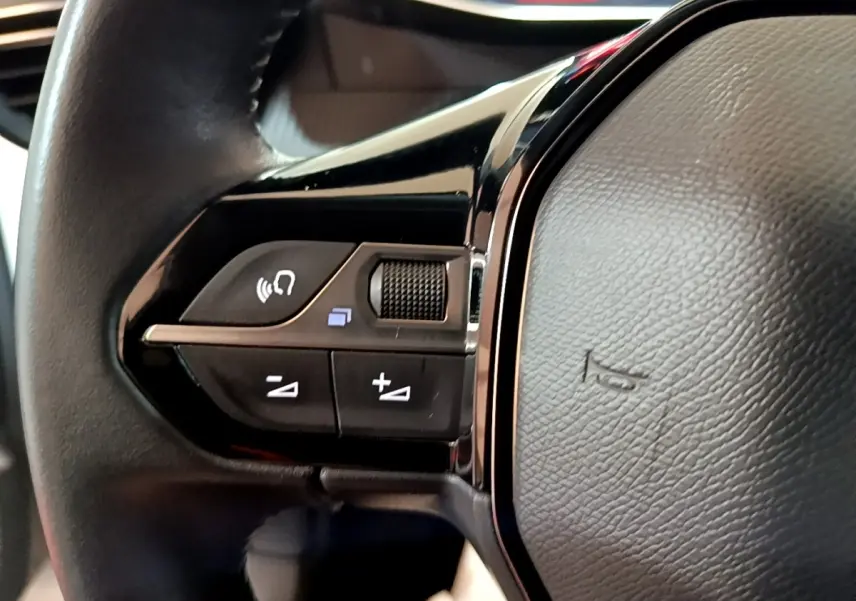 Gros plan sur les commandes gauche du volant cuir noir de la Peugeot 208 blanche, version PureTech 100 S&S Allure Business.