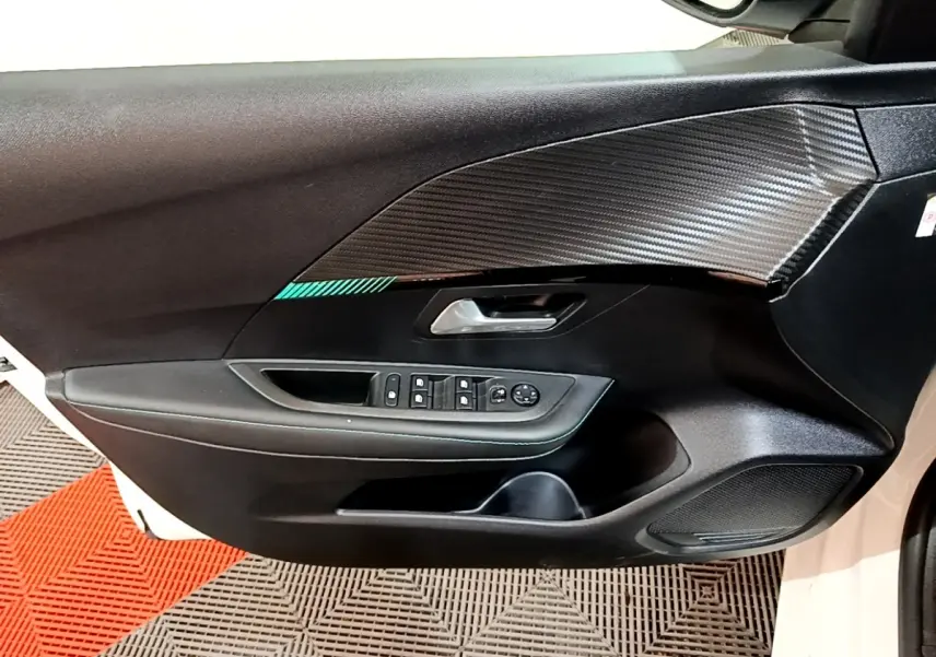 Vue intérieure côté gauche de la porte avant blanche d'une Peugeot 208 avec garniture noire et commandes des vitres.