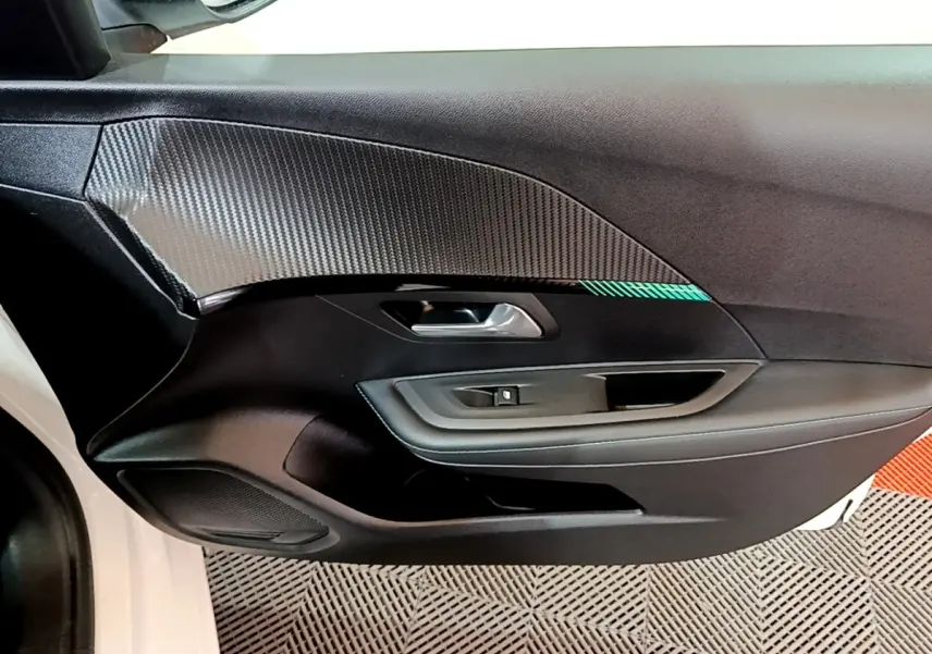 Vue rapprochée de la porte avant gauche blanche d’une Peugeot 208 2021 avec insert décoratif carbone et bouton lève-vitre.