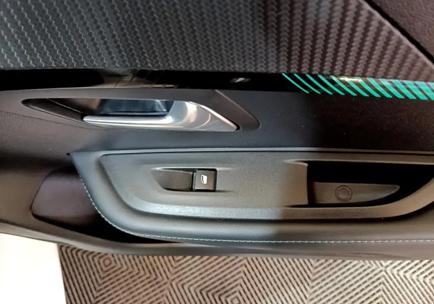 Gros plan sur la commande de lève-vitre et poignée intérieure côté gauche d’une Peugeot 208 blanche, finition Allure Business.