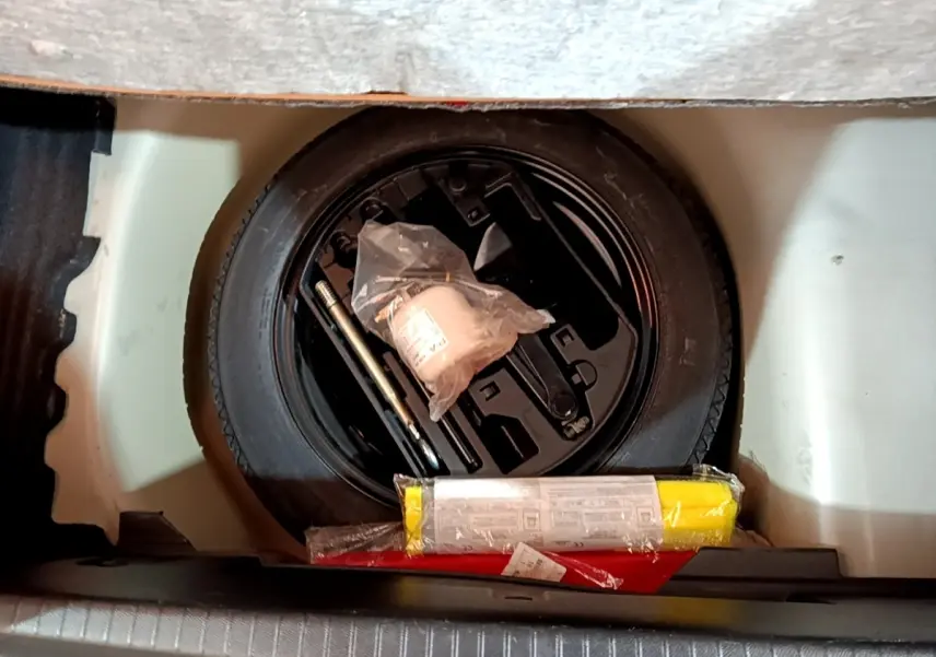 Vue plongeante sur la roue de secours noire et les outils de bord dans le coffre d'une Peugeot 208 blanche.