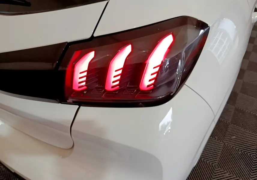 Gros plan sur le feu arrière droit rouge allumé d'une Peugeot 208 blanche, soulignant le design en griffes LED.