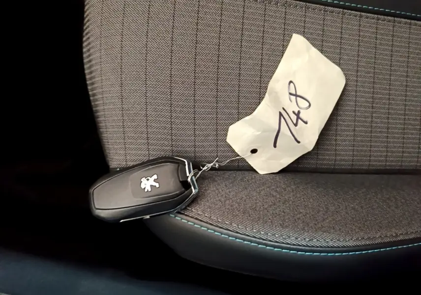 Clé de voiture Peugeot posée sur un siège tissu gris avec surpiqûres bleues, vue en gros plan intérieur.