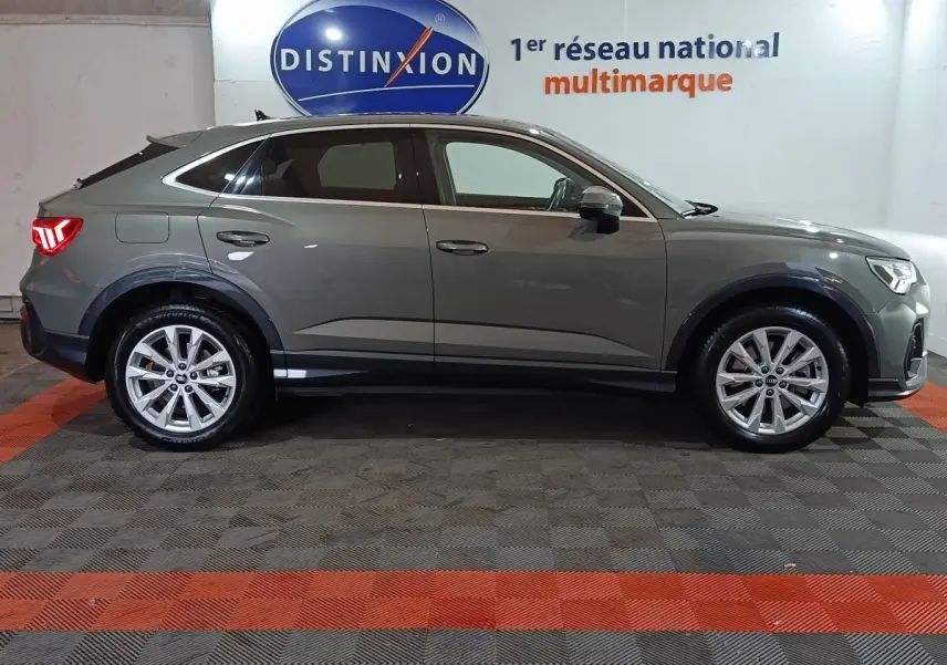 Profil droit d’un Audi Q3 Sportback gris foncé hybride rechargeable 2021, avec jantes alliage et feux arrière allumés.