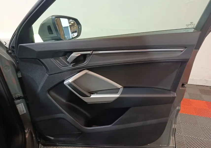Intérieur côté gauche de la porte avant d’un Audi Q3 Sportback gris foncé, avec poignée argentée et miroir latéral visible.