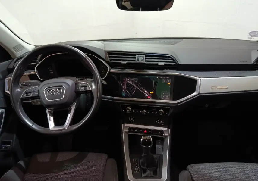 Vue intérieure avant de l'Audi Q3 Sportback gris foncé, mettant en valeur le volant cuir multifonctions et l'écran tactile central.