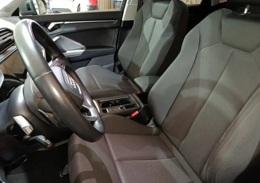 Vue intérieure côté conducteur de l'Audi Q3 Sportback gris foncé, montrant sièges tissu et volant cuir multifonctions.