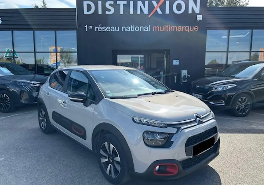 Citroën C3 sable métal vue 3/4 avant droit avec protections latérales noires et touches rouges sur pare-chocs.