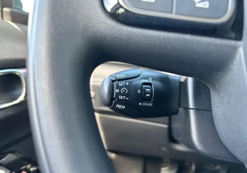 Gros plan sur la commande de régulateur de vitesse noire, située derrière le volant de la Citroën C3 sable métal.