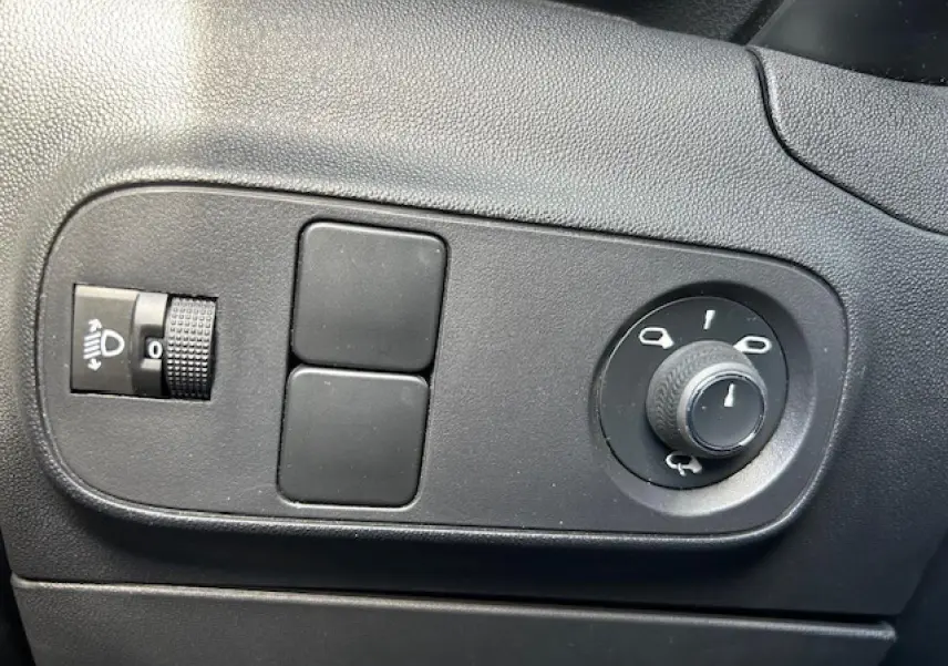 Gros plan sur les commandes noires de réglage des phares et des rétroviseurs dans une Citroën C3 sable métal de 2021.